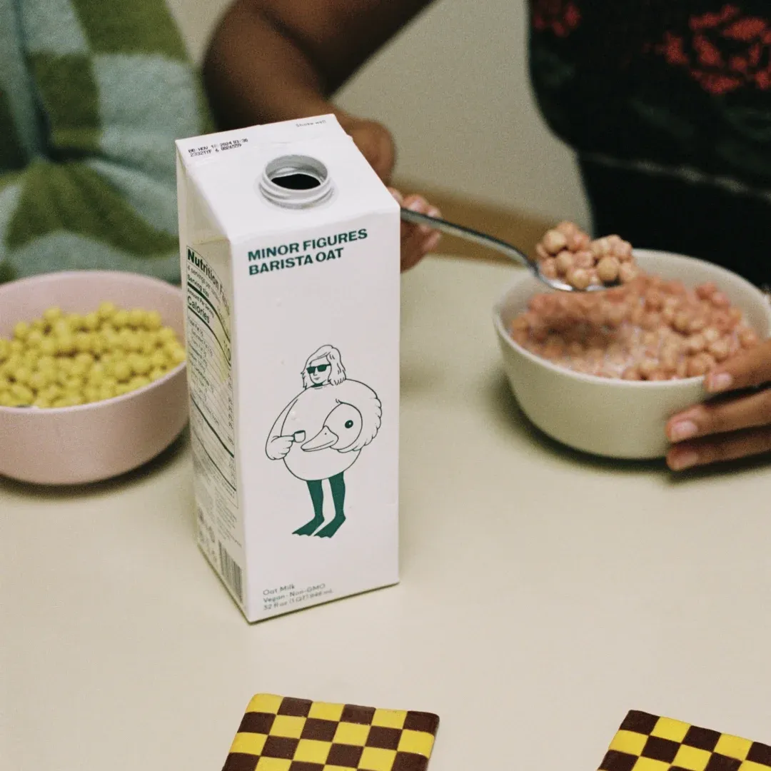 A picture of a Minor Figures oat milk carton and person eating cereal in the background